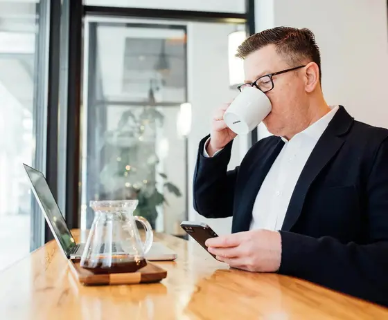 A person in a blazer reading a property report on a phone beside an open laptop