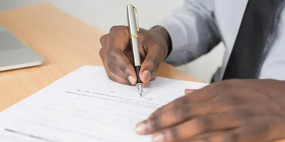 A person in a shirt and tie signing a recorded property document with a fountain pen